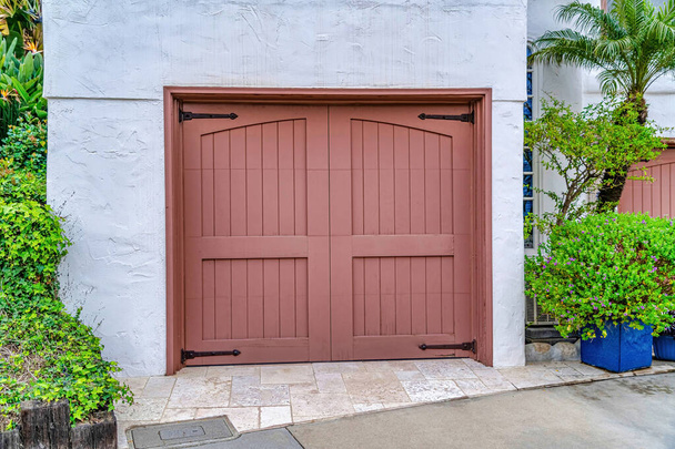 Facade of garage with brown wooden hinged door against white wall and foliage - Photo, Image