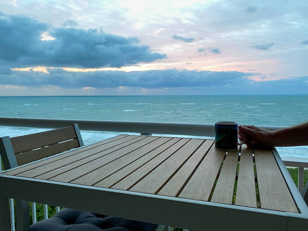 Uma xícara de café em uma mesa com um nascer do sol vibrante sobre o Oceano Atlântico em North Hutchinson Island, na Flórida, no fundo. - Foto, Imagem