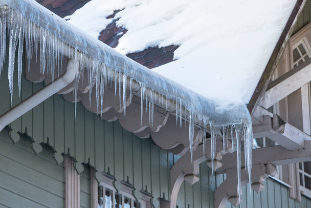 Estalactite de gelo pendurado no telhado com parede de madeira. Edifício coberto com grandes ciclones - Foto, Imagem