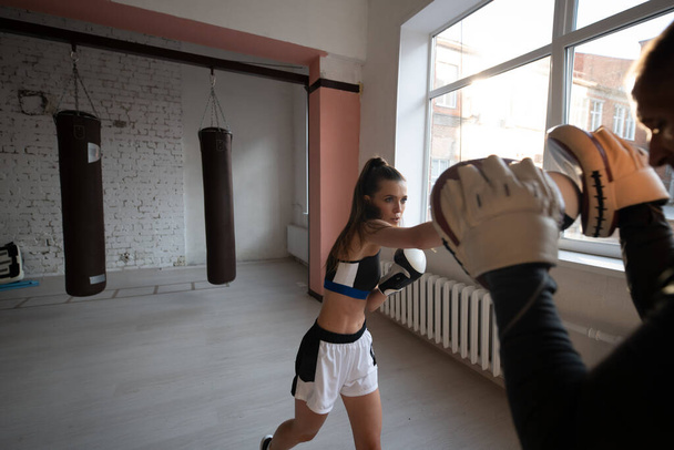 Mladá dívka diriguje trénink kickboxu a cvičí údery tlapkou s profesionálním boxerem - Fotografie, Obrázek