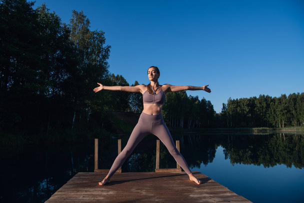 Junge Frau, die sich bei Sonnenuntergang am See entspannen will, schadet ausgestreckt. Yoga am Morgen am Waldsee. - Foto, Bild