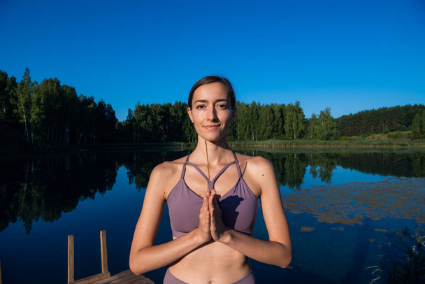 Femme faisant du yoga et méditant dans un lever de soleil à l'extérieur, tenant un bâton d'arôme dans ses mains, paumes en geste namaste. - Photo, image