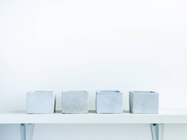 Чотири порожніх сучасних геометричних бетонних плантатора на полиці з білого дерева ізольовані на білому тлі стіни з копіювальним простором. Цементні горщики, кубічна форма
. - Фото, зображення