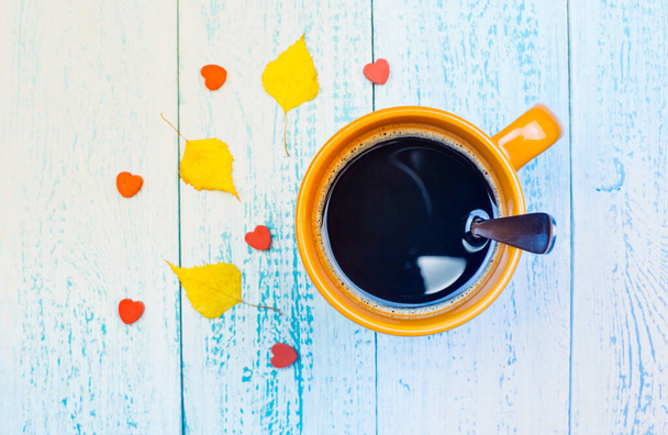 Чашка кофе с осенними листьями. Осенний фон. Кофе на синем фоне доски с желтыми падающими листьями и шишками. Hello, All. - Фото, изображение