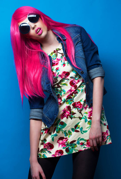 Young fashion female model with pink hair and big sunglasses over blue background - Photo, image
