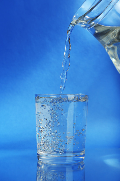 Pour water from  pitcher into  glass, on dark blue background - Foto, imagen