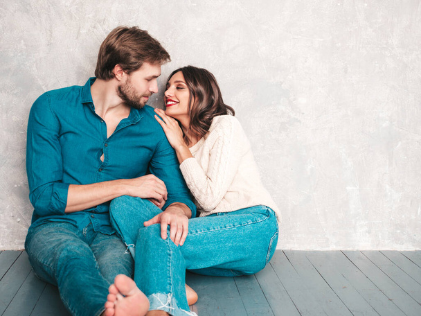 Smiling beautiful woman and her handsome boyfriend. Happy cheerful family sitting in studio on the floor near gray wall.Valentine's Day. Models hugging. Concept of love. Looking at each other - Fotó, kép