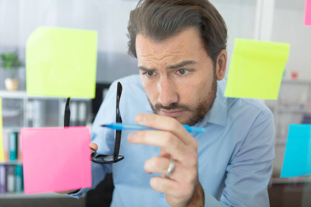thoughtful man reading sticky notes in office - Foto, afbeelding