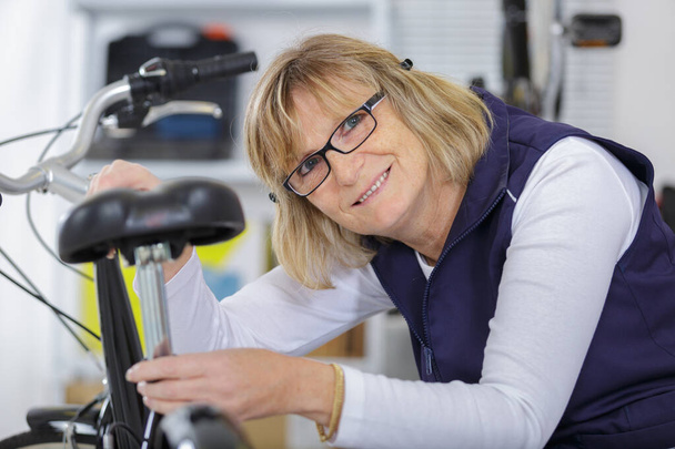 mature woman bike mechanic working on bicycle saddle - Fotografie, Obrázek