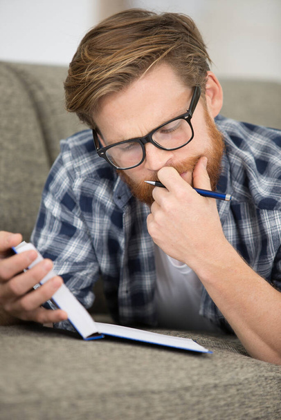 young man wearing eyeglasses reading a book on sofa - Foto, Bild