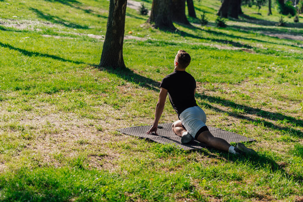 Gezonde jongeman doet het buiten opwarmen stretching oefeningen op een fitness mat - Foto, afbeelding