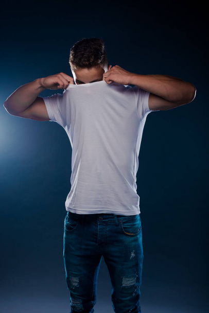 Studio fashion portrait of a young man wearing blue jeans, and white top - 写真・画像