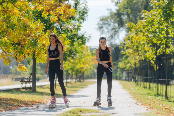Full-length picture of sexy sportswomen rollerskating in the park - Photo, Image