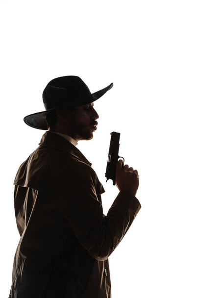 Retrato de un guapo tipo de silueta con sombrero sosteniendo pistola aislada sobre fondo blanco - Foto, imagen