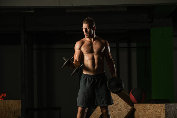 Zavřít tmavý portrét mladého muže bez košile cvičení činka střídavý biceps curl - Fotografie, Obrázek