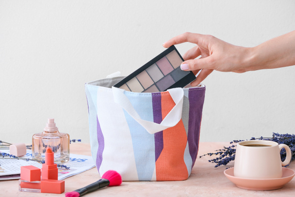 Mano y bolso femenino con cosméticos decorativos en la mesa - Foto, Imagen