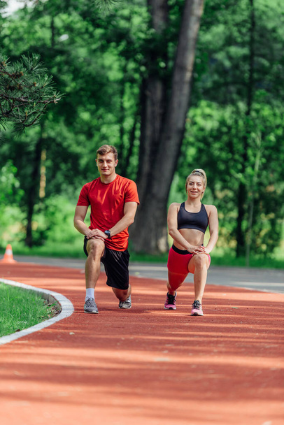 Young couple stretching before starting their morning jogging routine on a tartan track at the park. - Foto, immagini
