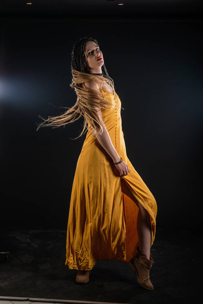 Містична древня королева-богиня в жовтій сукні на ізольованому чорному студійному тлі. Жіночий фемініст одягнений в коси і позує в студії
. - Фото, зображення