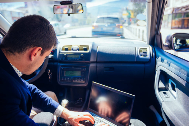 Vakmerő üzletember vezet a városban a csúcsforgalomban, miközben gépel a laptopján, és stresszesen viselkedik munka közben.. - Fotó, kép