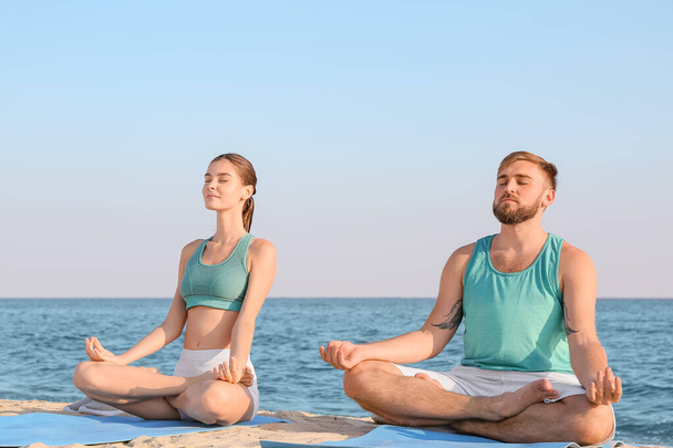 Sporty young couple practicing yoga on sea beach - Foto, Imagem