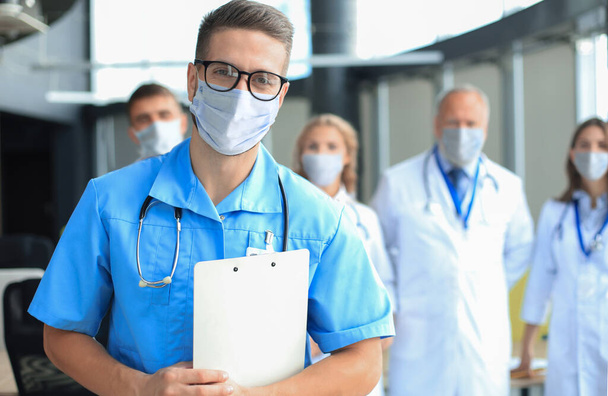 Médico masculino en máscara médica con grupo de colegas felices y exitosos también en máscaras preventivas. - Foto, Imagen