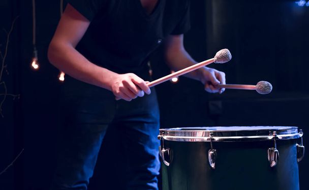 The percussionist plays with sticks on the floor tom in a dark room with beautiful lighting. Concert and performance concept. - Φωτογραφία, εικόνα