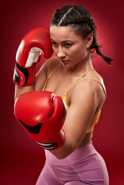 Young female boxer with red gloves on red background - Fotoğraf, Görsel
