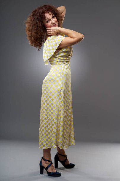 Beauty at 50. Studio portrait of a mature curly haired woman in long dress - Photo, Image