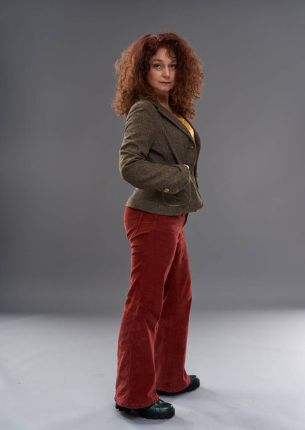 Curly redhead mature woman portrait, studio shot on gray background - Photo, image