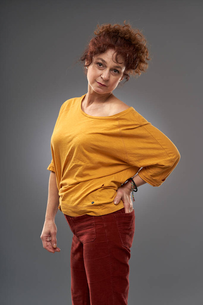 Curly redhead mature woman portrait, studio shot on gray background - 写真・画像