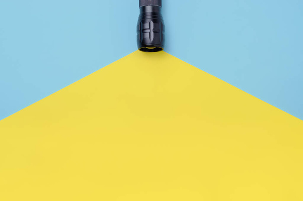 Flashlight turned on with yellow beam light on blue background with empty place for text. Top view - Photo, Image