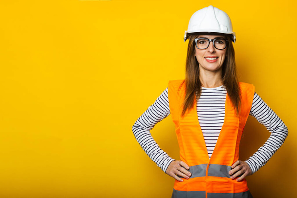 Junge Frau mit einem Lächeln in Weste und Hut auf gelbem Hintergrund. Baukonzept, Neubau. Banner. - Foto, Bild