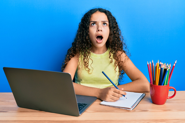 Teenager hispánská dívka sedí na stole a učí se do školy naštvaný a šílený křičí frustrovaný a zuřivý, křičí vzteky vzhlíží.  - Fotografie, Obrázek