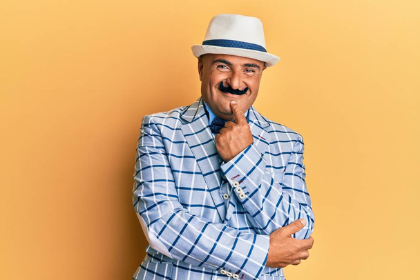 Homme mûr du Moyen-Orient avec une moustache vêtue d'un style vintage et élégant regardant avec confiance la caméra avec le sourire avec les bras croisés et la main levée sur le menton. penser positivement.  - Photo, image