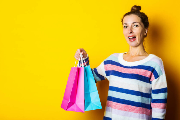 Young woman in sweater holding shopping bags on yellow background. - Photo, Image