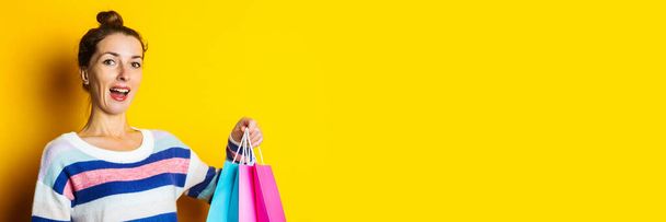 Young woman in sweater holding shopping bags on yellow background. - Photo, Image