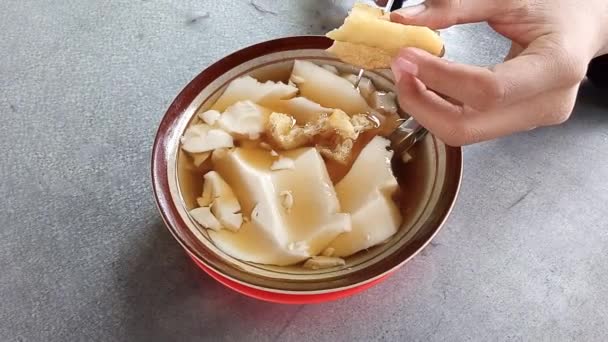 крупным планом китайская сладкая традиционная еда называется Douhuwa таува бобы творог тофу пудинг с горячим имбирным сиропом и показывая руку резки лук жареный хлеб пирог с ножницами - Кадры, видео