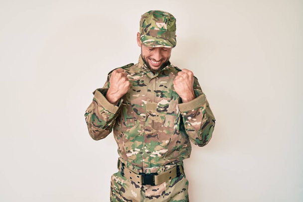 Jovem caucasiano vestindo uniforme do exército de camuflagem animado para o sucesso com os braços levantados e os olhos fechados celebrando a vitória sorrindo. conceito vencedor.  - Foto, Imagem