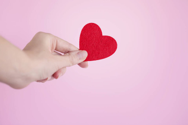 Weibliche Hand mit rotem Herz auf rosa Hintergrund. Das Konzept der aufrichtigen Hingabe an den Glauben. Spende, Lebensrettung oder Wohltätigkeitskonzept. Valentinstag. Muttertag - Foto, Bild