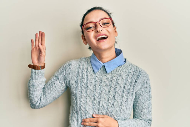 Młoda kaukaska kobieta w luźnych ubraniach i okularach rezygnuje witając szczęśliwy i uśmiechnięty, przyjazny gest powitalny  - Zdjęcie, obraz