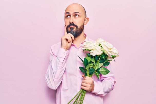 Mladý pohledný muž držící květiny vážný obličej přemýšlející o otázce s rukou na bradě, přemýšlivý o matoucím nápadu  - Fotografie, Obrázek