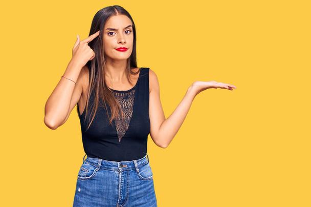 Mujer hispana joven vestida con ropa casual confundida y molesta con la palma abierta mostrando espacio para copiar y señalando con el dedo a la frente. Piénsalo.  - Foto, Imagen
