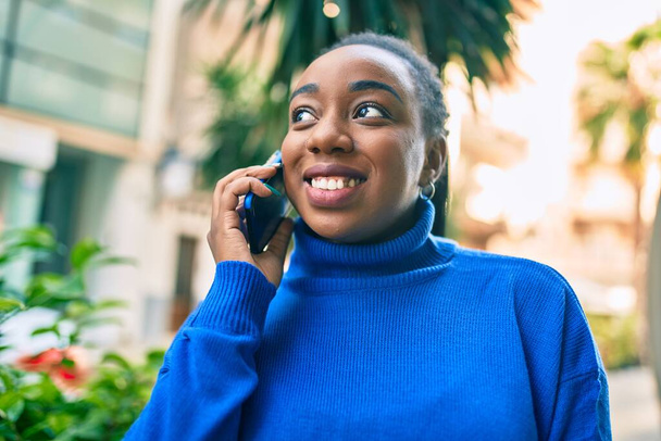 Młoda Afroamerykanka uśmiecha się szczęśliwa rozmawiając na smartfonie w mieście. - Zdjęcie, obraz