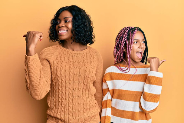 Bella madre e figlia afroamericana che indossano maglione invernale in lana sorridente con viso felice guardando e indicando il lato con pollice in su.  - Foto, immagini