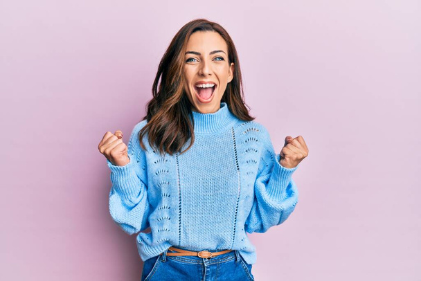 Young brunette woman wearing casual winter sweater over pink background celebrating surprised and amazed for success with arms raised and open eyes. winner concept.  - Photo, Image