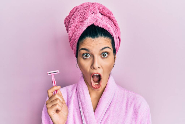 Nuori latino nainen yllään suihku kylpytakki tilalla partaveitsi peloissaan ja hämmästynyt suu auki yllätys, epäusko kasvot  - Valokuva, kuva