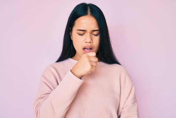 Молодая красивая азиатская девушка в случайном розовом свитере чувствует себя нездоровым и кашляет как симптом от холода или бронхита. концепция здравоохранения.  - Фото, изображение