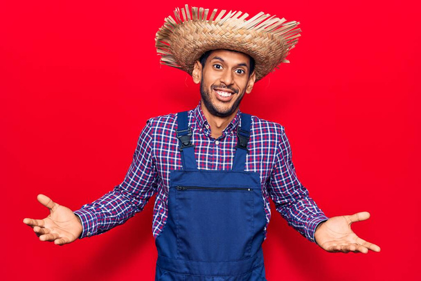 Nuori latinomies yllään maanviljelijä hattu ja esiliina tietämätön ja sekava ilme kädet ja kädet ylhäällä. epävarma käsite.  - Valokuva, kuva