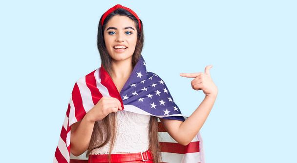 Barna tinédzser lány gazdaság Egyesült Államok zászló ujjal mutogatott egy önmosolygó boldog és büszke  - Fotó, kép