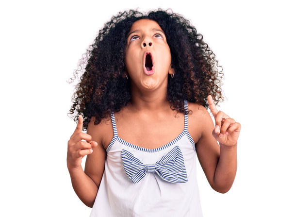 African american child with curly hair wearing casual clothes amazed and surprised looking up and pointing with fingers and raised arms.  - Foto, Imagem